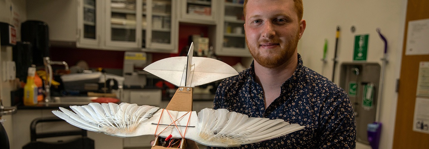 Student holds a model of an ancient style of flying machine