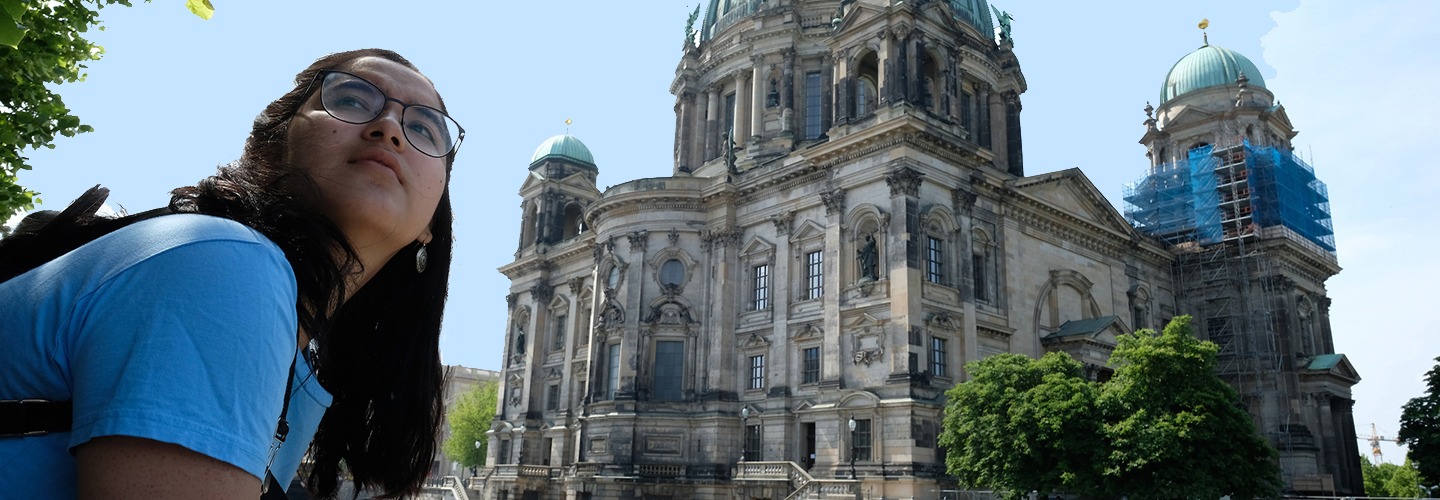 A student in a blue shirt looks back over her shoulder. In the background is an ornate building