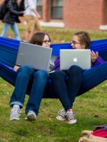 Two students sit in a hammock with their laptops.