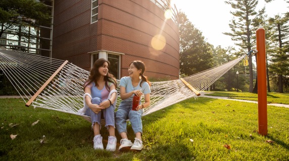 2 students talk while sharing a hammock on central campus