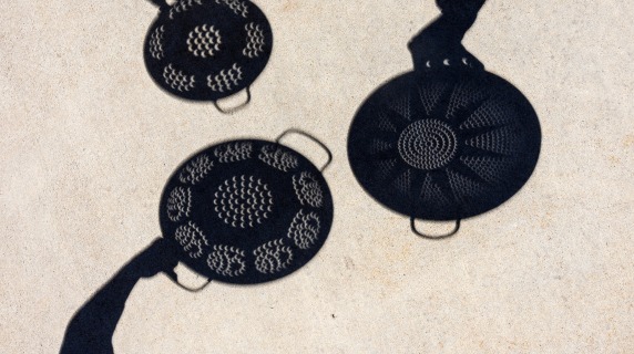 Shadows of colanders on the sidewalk working as pinhole cameras to view the shadow of the moon crossing the sun