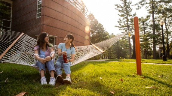 Two students sit in a hammock, talking.