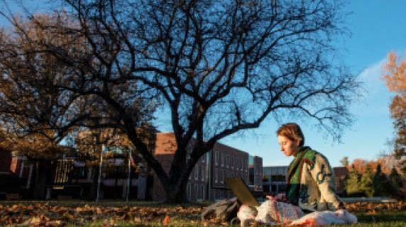 Student sitting on the grass, reading.