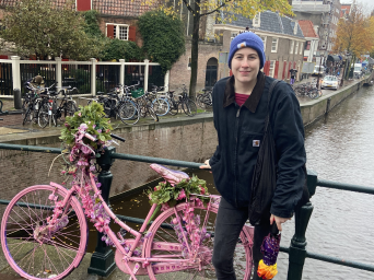 Sophia leans next to a railing and a pink bike. There is a river underneath her.