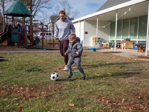 child plays soccer with caregiver at preschool playground