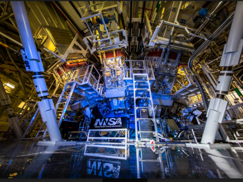 A large, circular atrium houses machinery used to measure the results of laser experiments in the interior chamber. The atrium is awash in blue light, and a banner on the central chamber reads National Nuclear Security Administration.