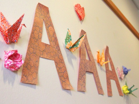 Picture of AAA cut out letters taped on a white wall full of origami.