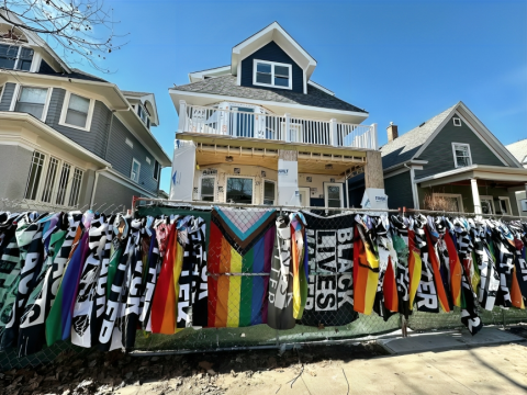 A house under construction and surrounded by fences. The fence is covered by Pride and Black Lives Matter flags.