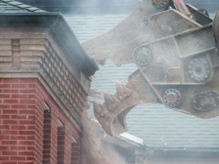 Heavy machinery kicks up a cloud of dust as it destroys part of a roof.