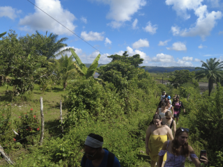 A line of students trek uphill through lush foliage in the Brazilian countryside. The sky is blue and dotted with clouds.