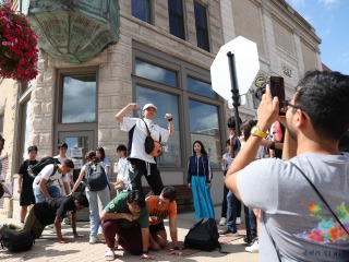 Multiple students build a pyramid, leaving one student to pose on top. Another student takes a picture.