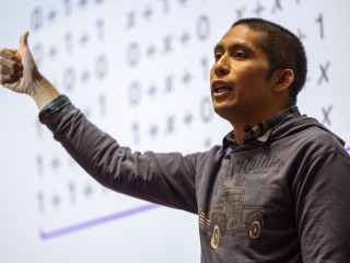 Peter-Michael Osera stands in front of a slide of equations with a thumbs up gesture