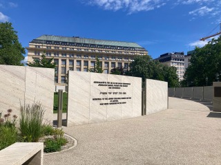 An oval of stone slabs carved with the names of Austrian Holocaust victims under a blue Vienna sky