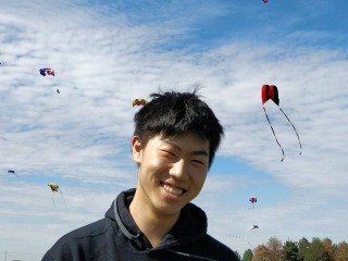 Ryuta smiles in foreground with sky full of kites behind