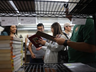 Students chatting and looking at books in the background, with shelf in the foreground