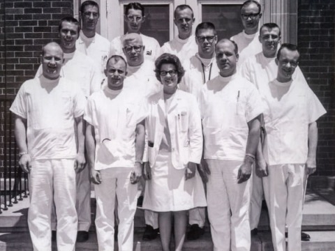 JoEllen Hoth and twelve other doctors in white scrubs stand on the front step of a hospital.