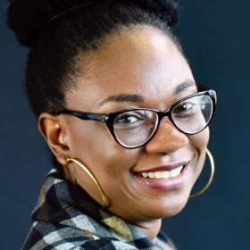 A Black woman with glasses and hoop earrings smiles at the camera.