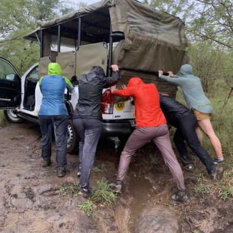 Five women in rain gear push a truck out of a muddy ditch.