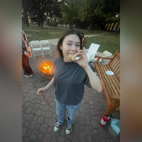 A girl takes a munch out of a smore outside a campus dorm bonfire.