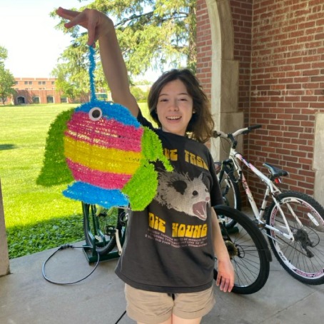 A young Hispanic woman holds a paper fish art project.